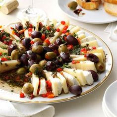 a platter filled with olives and cheese on top of a white table cloth