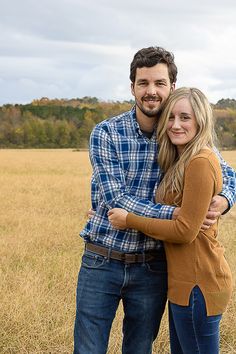 a man and woman are standing in the middle of an open field with their arms around each other