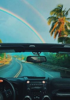 a car driving down a road with a rainbow in the sky and palm trees behind it