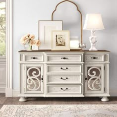 a white dresser with flowers and pictures on it next to a lamp in a room