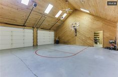 an indoor basketball court in the middle of a large room with two garage doors open