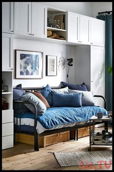 a day bed with blue sheets and pillows in a room filled with white cupboards