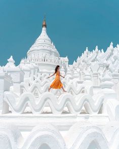 a woman in an orange dress is jumping on a white building with arches and spires