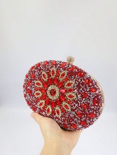 a hand holding a red and gold clutch bag with sequins on it's side