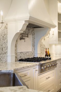 a kitchen with white cabinets and marble counter tops, an oven hood over the stove