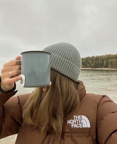 a woman wearing a beanie and holding a cup in front of her face with the north face logo on it