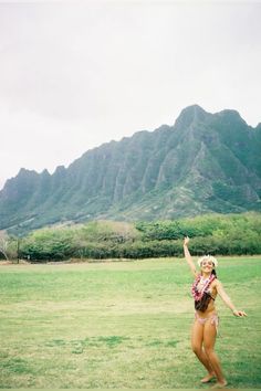 a woman standing on top of a lush green field next to a large mountain range