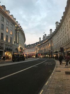 an empty city street at dusk with people walking on the sidewalk and cars driving down it