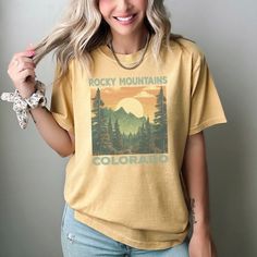 Explore in style with this Vintage Rocky Mountains Colorado T-Shirt. Perfect for the outdoor enthusiast, this graphic tee features a beautiful sun-soaked landscape of the Rocky Mountains that will inspire your next adventure. Made with soft, breathable fabric, it's ideal for both hikes and casual wear. Unisex sizing makes it a great fit for anyone, while the stunning design serves as a charming gift for travelers or nature lovers. Please remember to wash inside out and tumble dry, do not use ble Sublimation Print Tops For Summer Outdoor, Summer Tops With Sublimation Print For Outdoor, Summer Outdoor Tops With Sublimation Print, Summer Outdoor Top With Sublimation Print, Summer Graphic Print Tops For Outdoor Activities, Graphic Print Tops For Outdoor Summer Activities, Graphic Print Tops For Summer Outdoor Activities, Summer Graphic Tee For Outdoor, Graphic Tee Tops For Outdoor Summer Activities