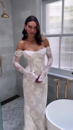 a woman in a white wedding dress standing next to a bathtub with her hands on her hips