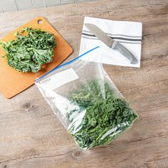 a bag of greens next to a knife on a cutting board