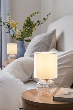 a table lamp sitting on top of a bed next to a vase with flowers in it