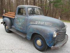 an old blue truck parked in a parking lot next to some trees and bushes with writing on the side