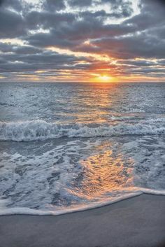 the sun is setting over the ocean with waves coming in to shore and some clouds