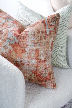 two pillows sitting on top of a white chair next to a pillow with an orange and blue pattern