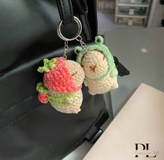 two crocheted stuffed animals hanging from a black leather handbag on a table