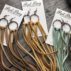 three pairs of leather tassels with metal hooks on wooden table next to business cards