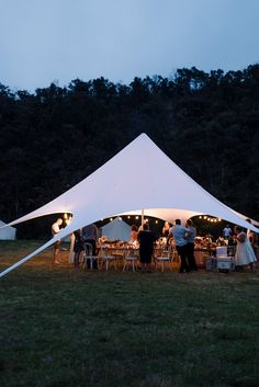 a group of people standing under a white tent at night with lights on the tables