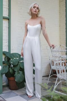 a woman standing in front of a brick wall wearing white pants and a strapless top