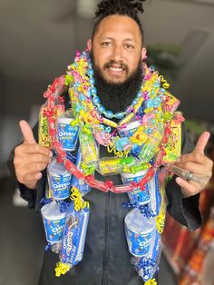 a man with a beard wearing a lei and holding up two cans of sodas