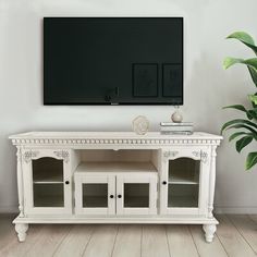 a white entertainment center with glass doors and drawers in front of a flat screen tv