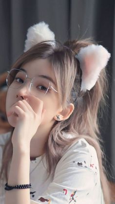 a girl wearing glasses and cat ears with her hand on her chin looking at the camera