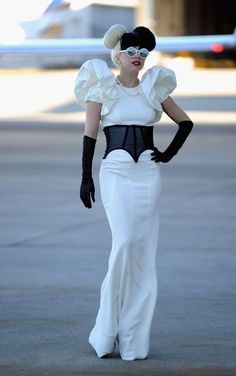 a woman in a white dress and black gloves is standing on the tarmac with her hands on her hips