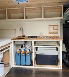 an rv kitchen with two coolers under the counter and storage space below for camping gear