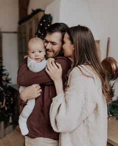 a man and woman holding a baby in front of a christmas tree