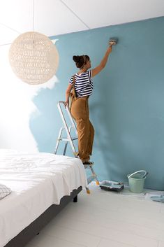 a woman on a ladder painting the wall in her bedroom with blue paint and white walls