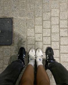 two people standing next to each other on a tiled floor with their legs crossed and one person wearing white sneakers