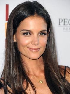 a woman with long brown hair wearing a black dress and gold necklace smiling at the camera