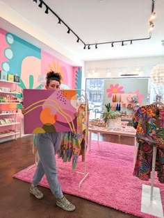 a woman holding up a piece of art in front of a pink carpeted room