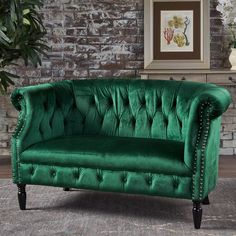 a green velvet couch in front of a brick wall with potted plants on it