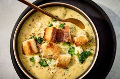 a bowl of soup with tofu, broccoli and cheese in it next to a spoon