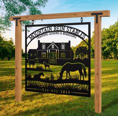 a sign that is in the grass with horses and houses behind it on a sunny day