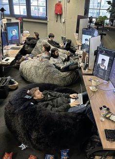 a group of people sitting on bean bag chairs in an office with computers and other items