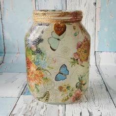 a jar with flowers and butterflies painted on it sitting on a white wooden floor next to a blue wall