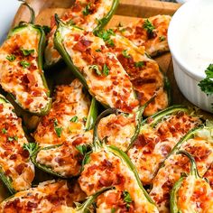 stuffed jalapenos with cheese and bacon are on a wooden tray next to a small bowl of ranch dressing