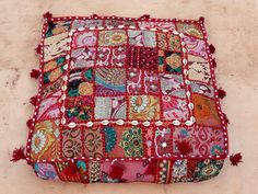 a patchwork cushion with tassels and beads on the bottom is laying on concrete