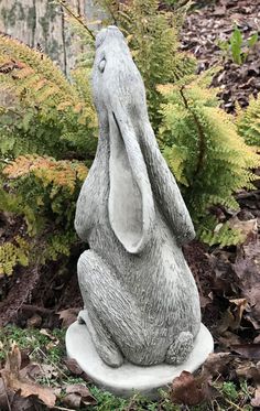 a statue of a rabbit sitting on its hind legs in the grass and bushes behind it