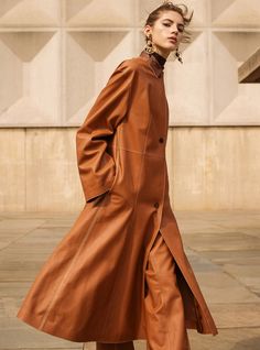 a woman in a brown coat is walking down the street with her hand on her hip