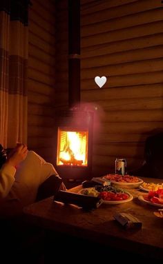 a person sitting in front of a fireplace with food on the table next to it