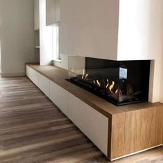 a modern fireplace in the middle of a room with wood flooring and white walls