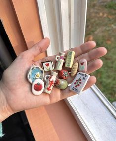 a person's hand holding small magnets in front of a window sill