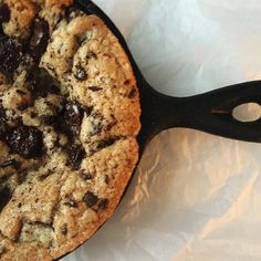 a chocolate chip cookie in a cast iron skillet on a white tablecloth background