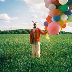 a man standing in the middle of a field holding balloons