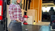 a woman is standing in the back of a van holding a driller and tool