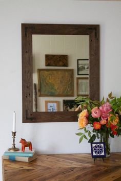 a vase with flowers on top of a wooden table next to a mirror and candle