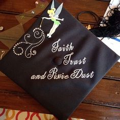 a black graduation cap with the words faith trust and shine dust on it sitting on top of a wooden table